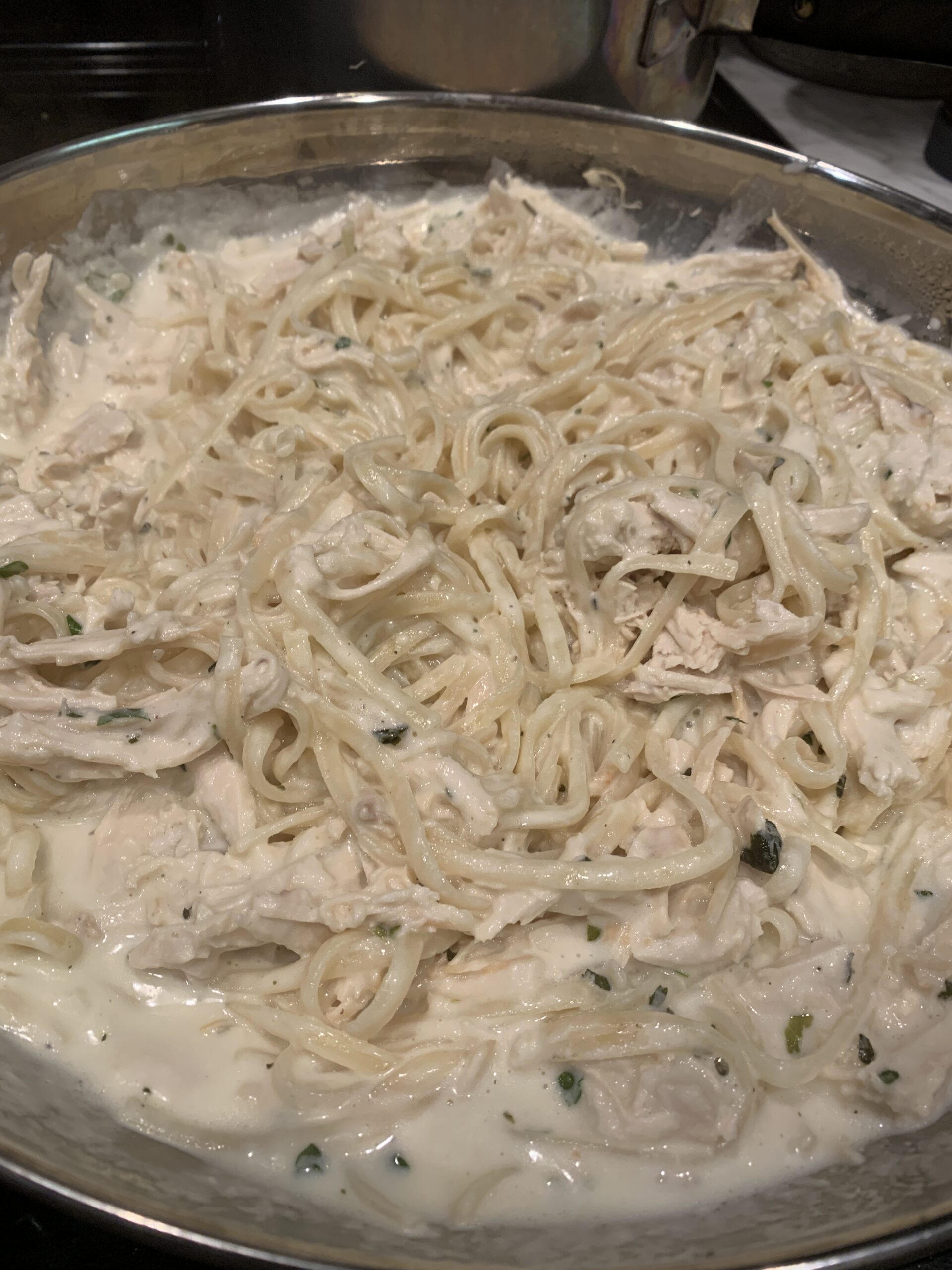 pan of alfredo sauce in linguine noodles with shredded chicken