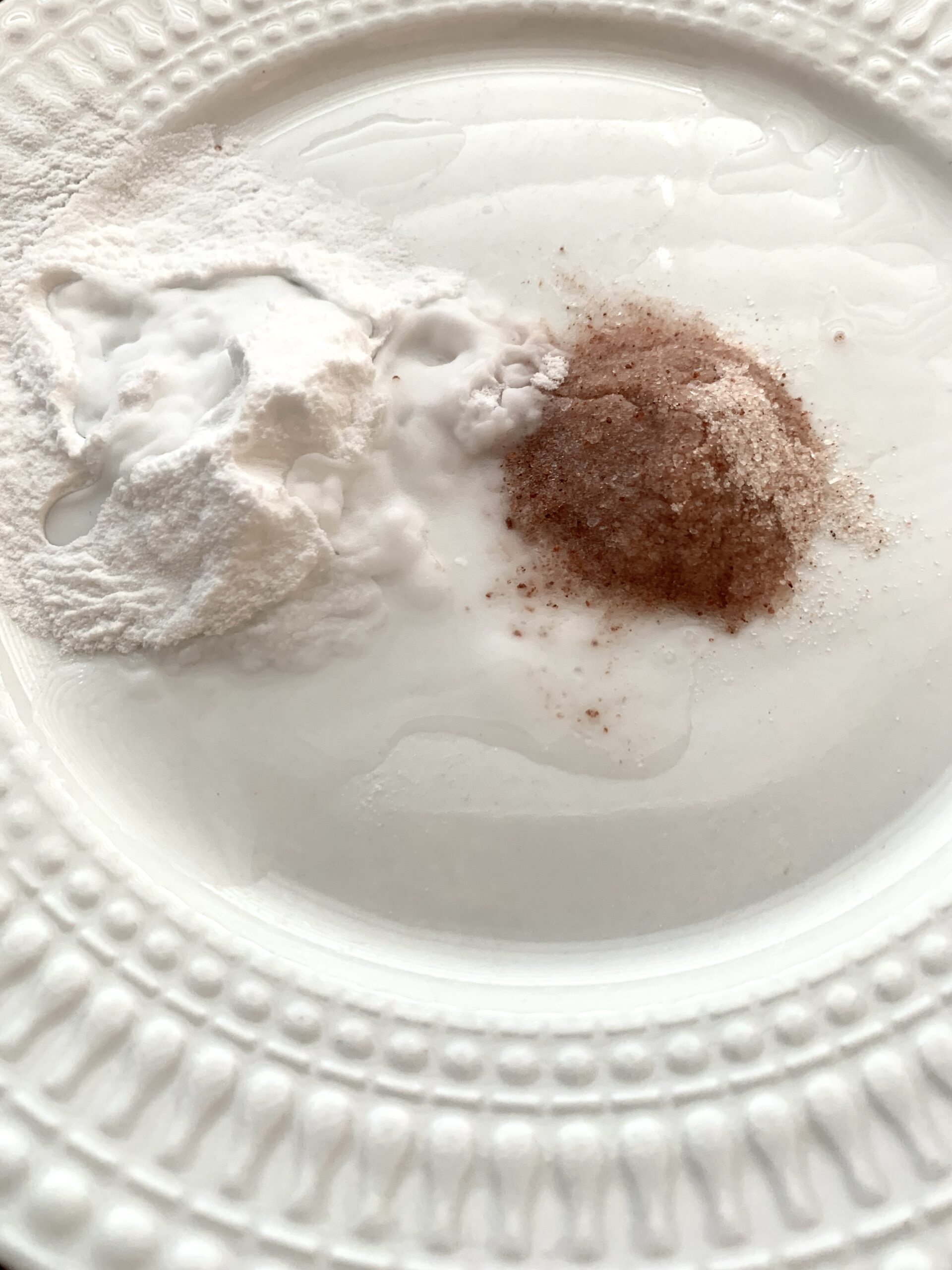 white round plate with piles of pink sea salt and baking soda with water on it to make face scrub