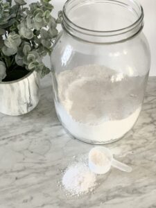 clear jar with white homemade dishwasher detergent with a eucalyptus plant in the background