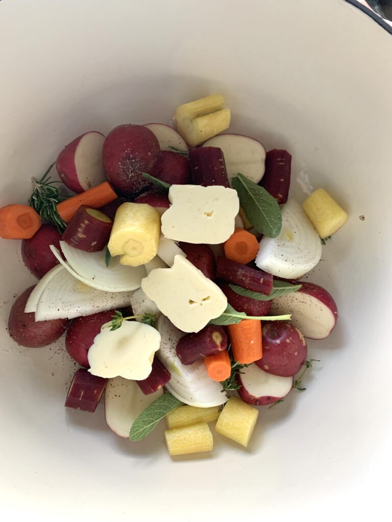 cut vegetables in a dutch oven with 3 pats of butter on top ready to be roasted