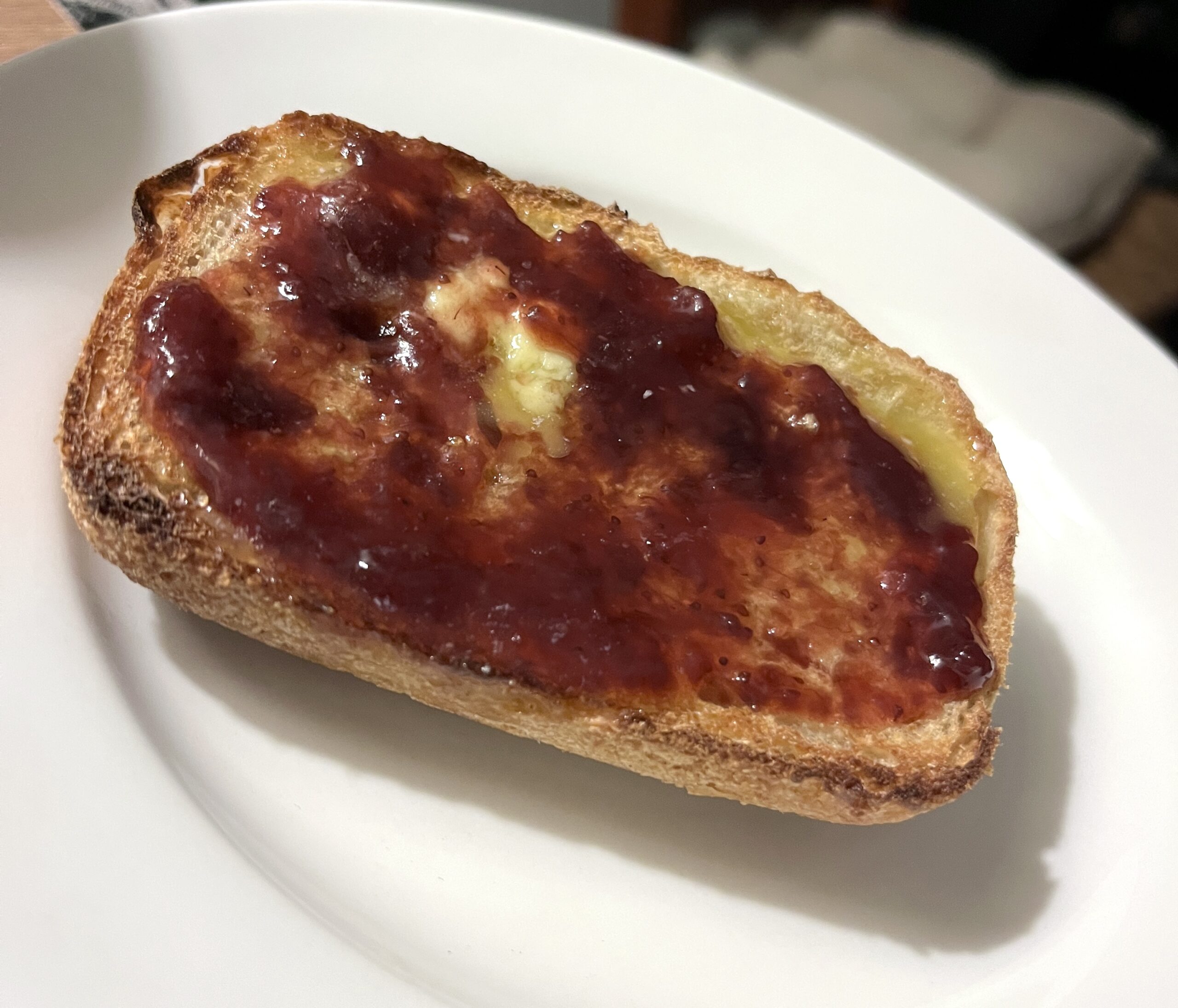 slice of sourdough toast with butter and strawberry jam on a white plate