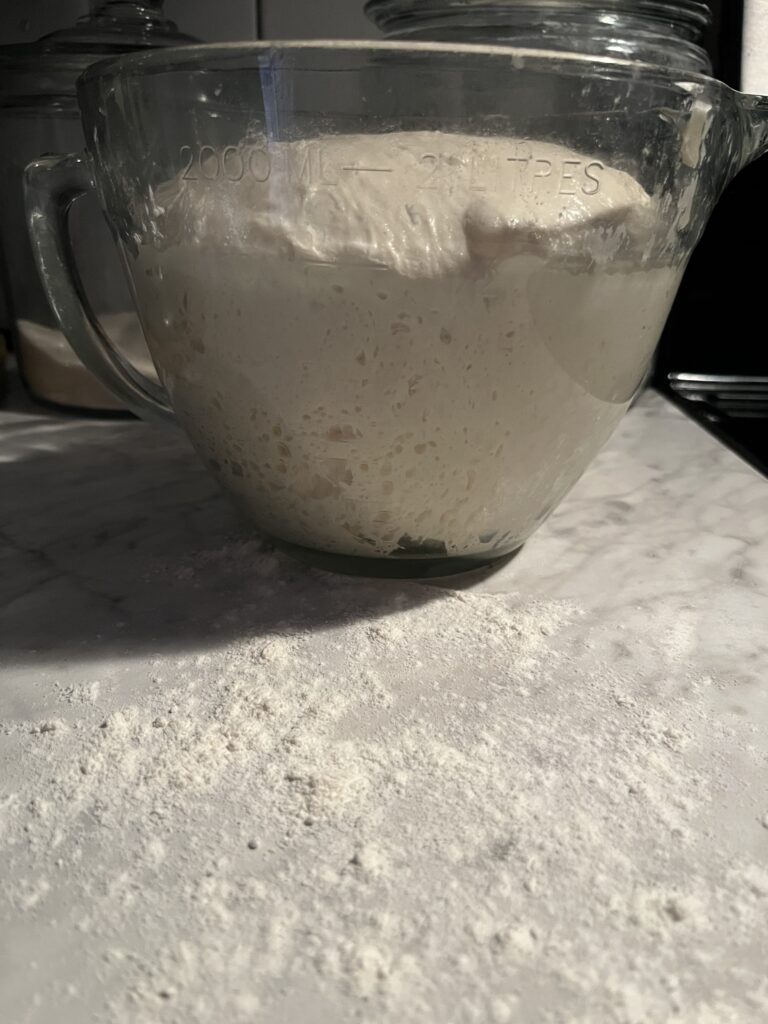 glass bowl sitting on a floured white marble counter with doubled in size no yeast sourdough bread dough