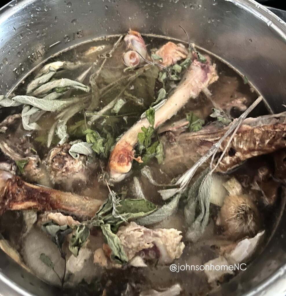 chicken bones and herbs in a stainless steel pot of water