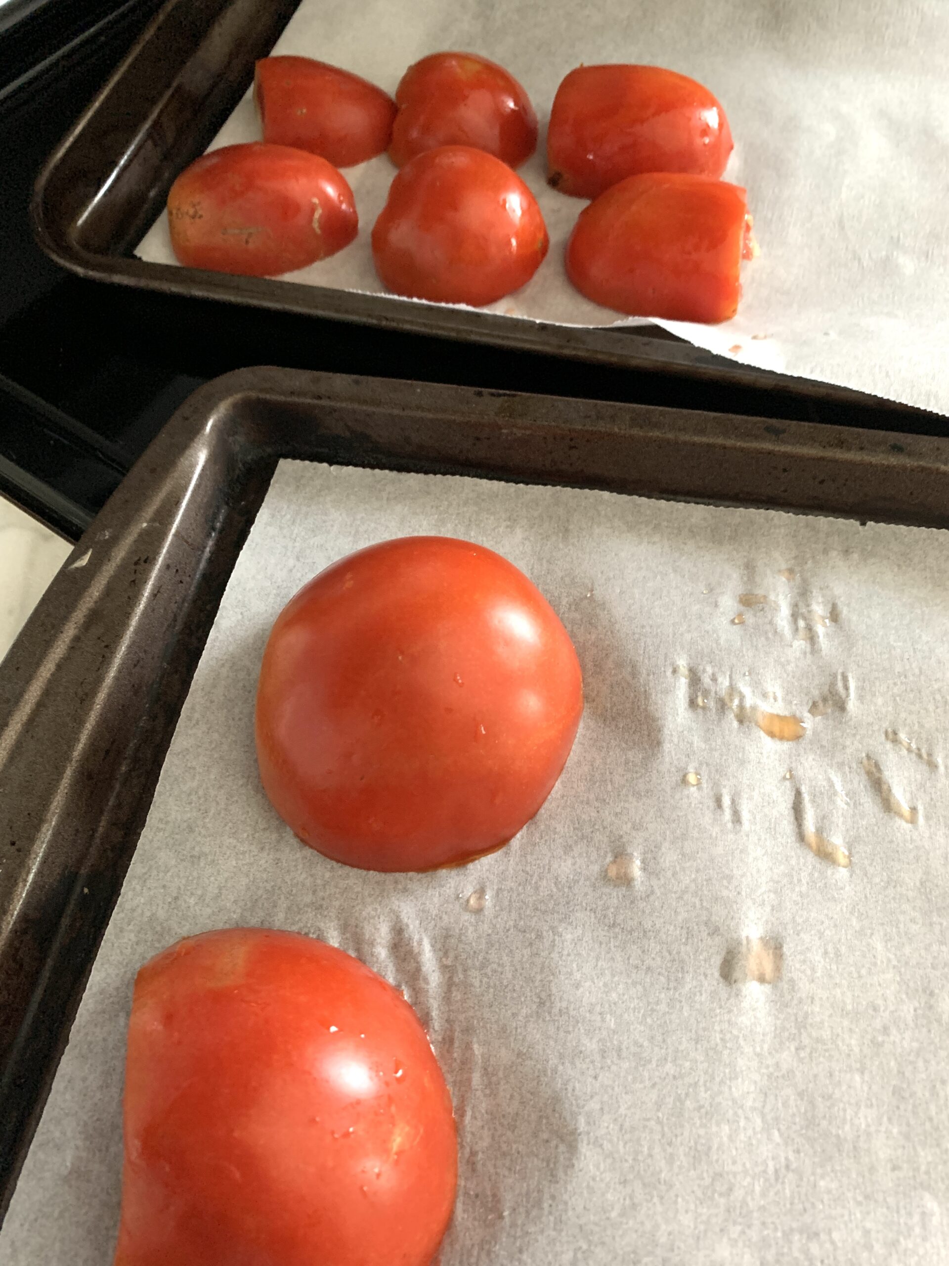 two cookie sheets lined with white parchment paper with tomato halves on them