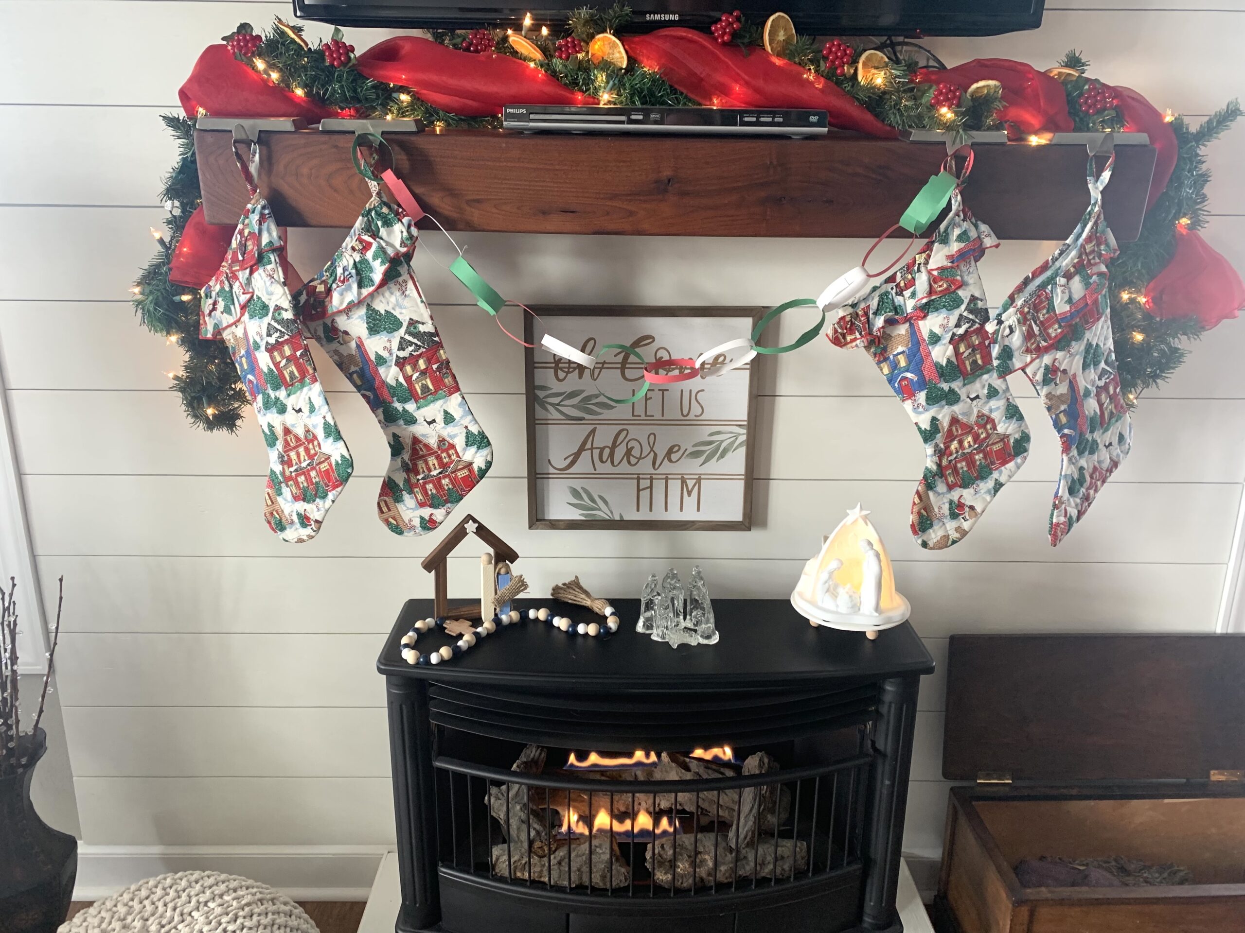 wooden mantle over lit black gas stove decorated for Christmas with greenery and orange slices