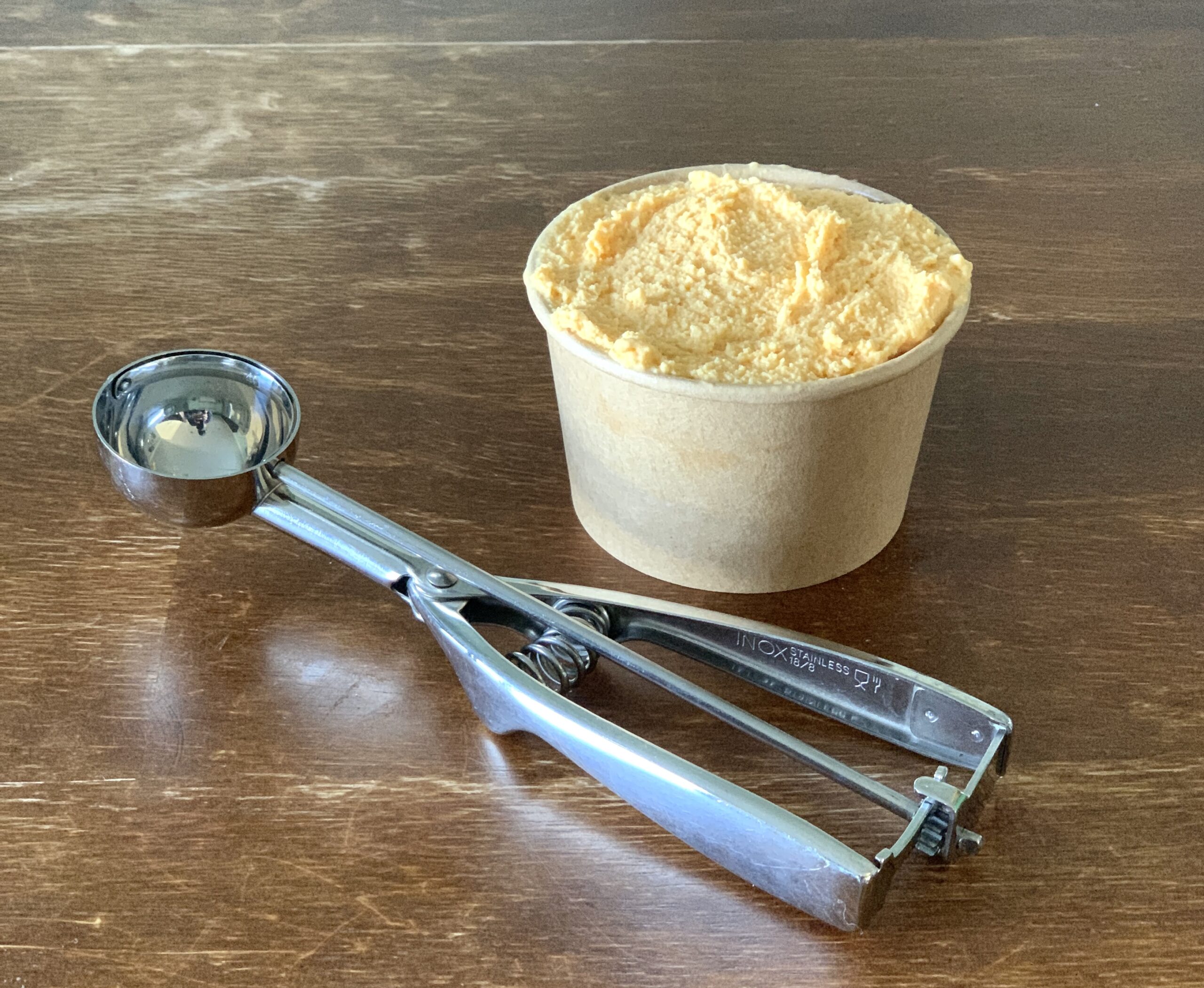 pumpkin cheesecake ice cream sitting on wooden table with a metal ice cream scooper beside it