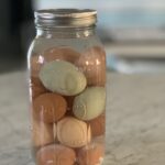 half gallon mason jar full of brown and blue eggs in water with pickling lime settled at the bottom of the jar on a marble counter top