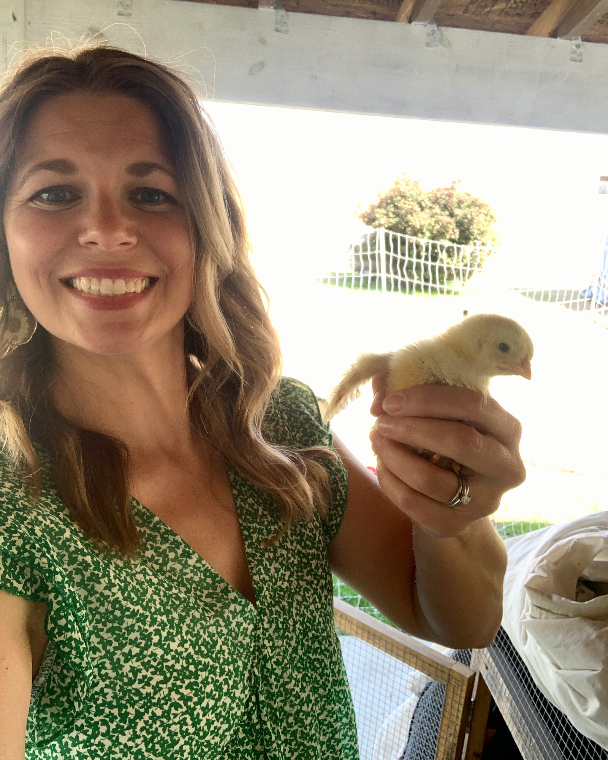 woman in green and white dress holding a yellow baby chicken in her hand by her face