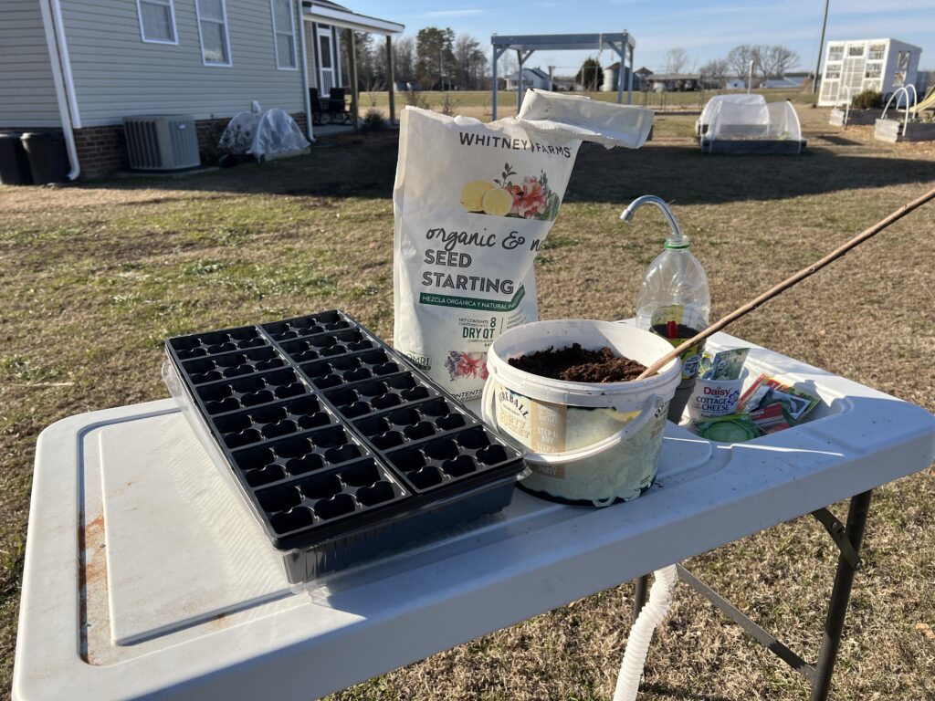 white table sitting outside on a sunny day in a yard with a seedling tray, small bucket, and seed starter soil