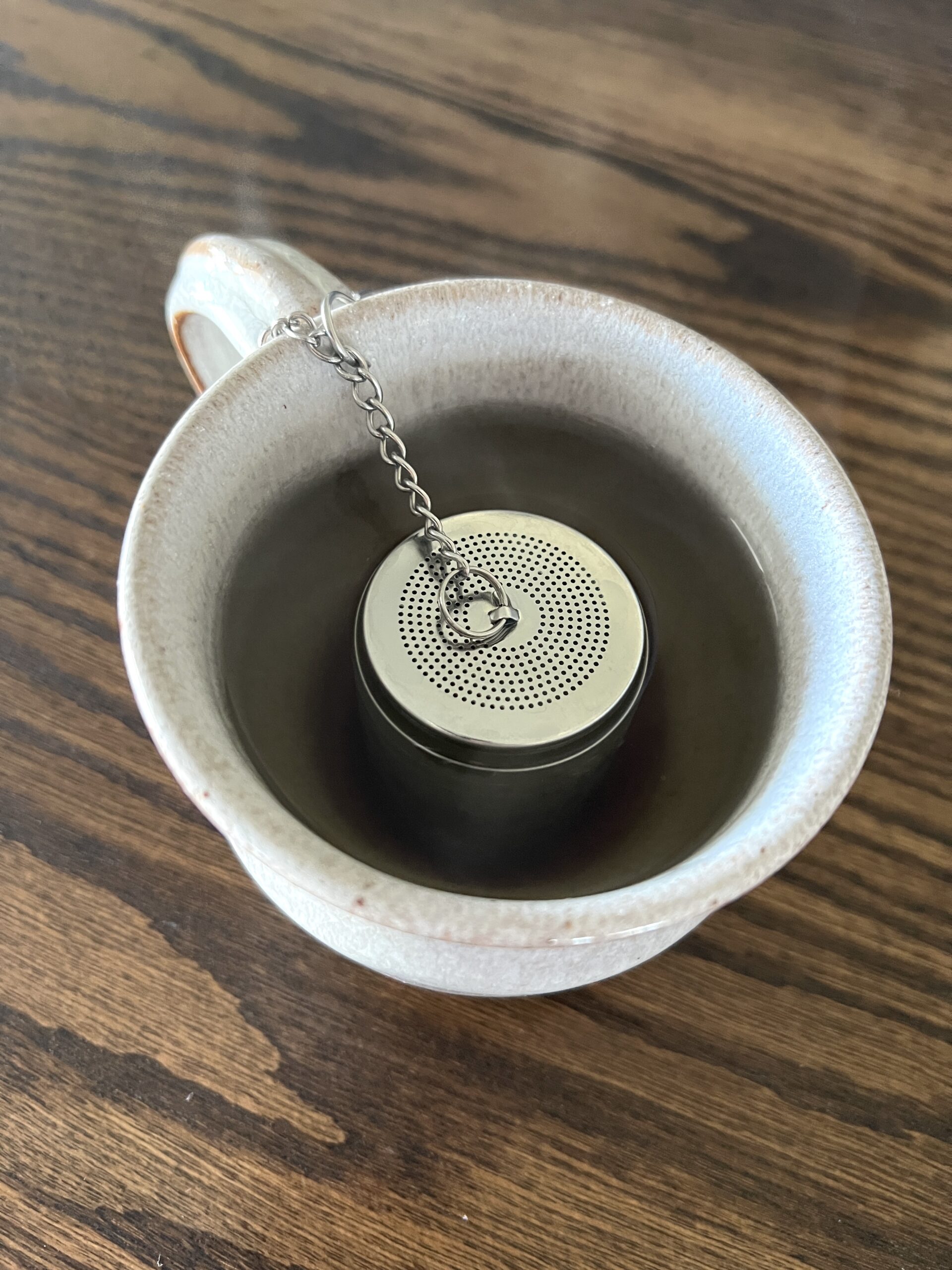 a white pottery mug full of water holding a silver tea steeper making elderberry tea