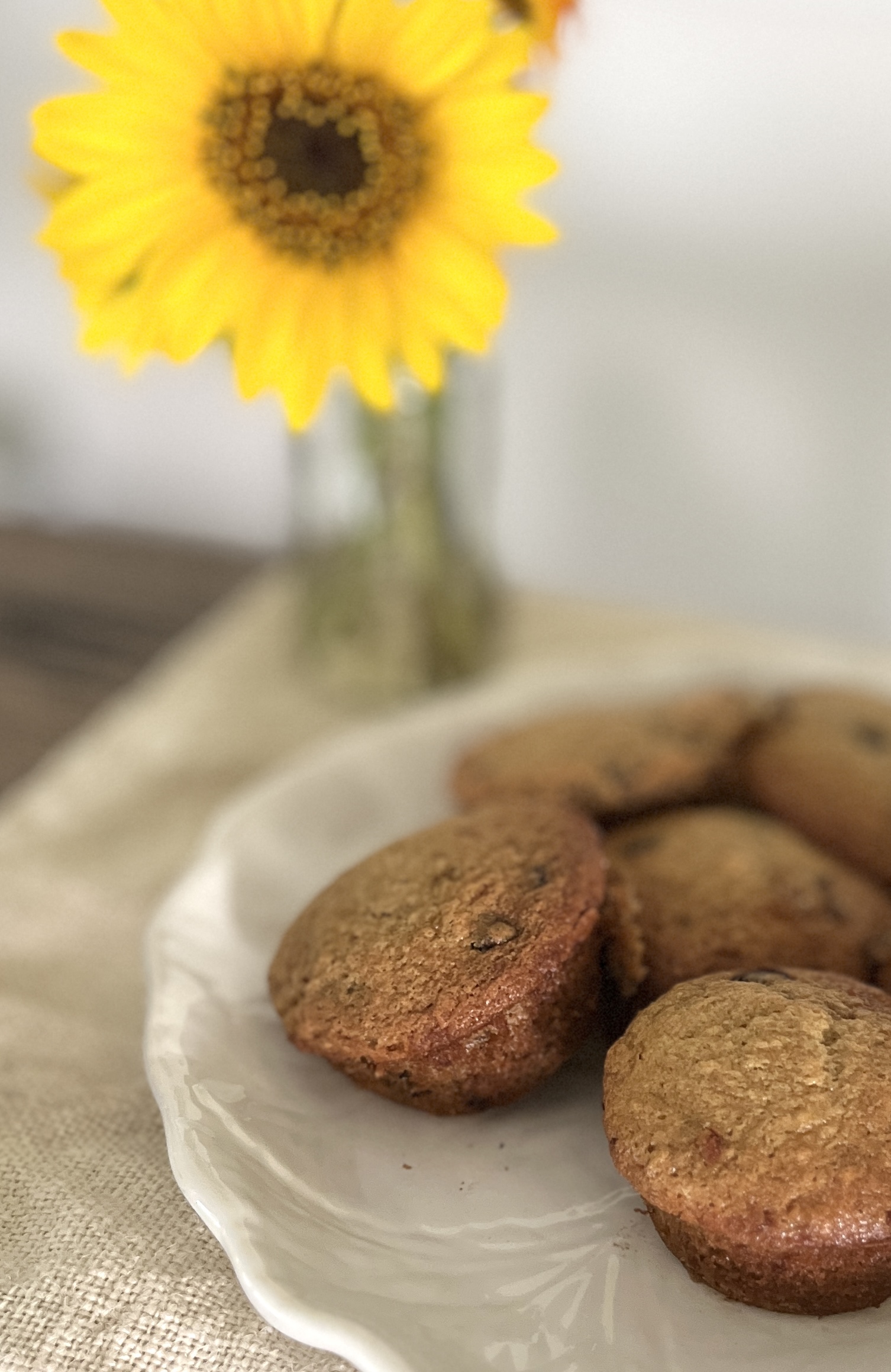 a white plate of banana chocolate chip muffins on a linen table setting with a sunflower in the background