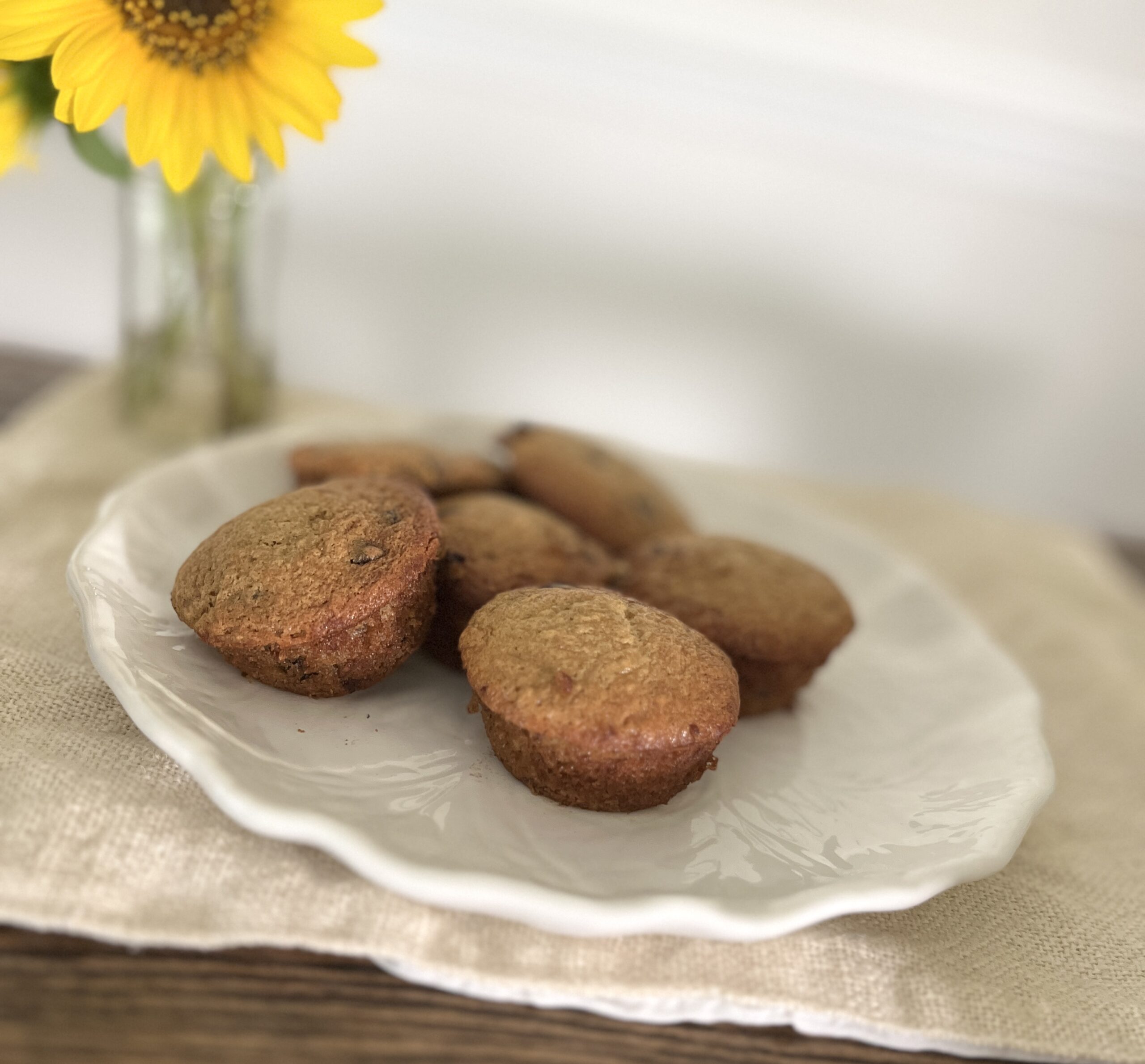 a white plate of banana chocolate chip muffins on a linen table setting with a sunflower in the background