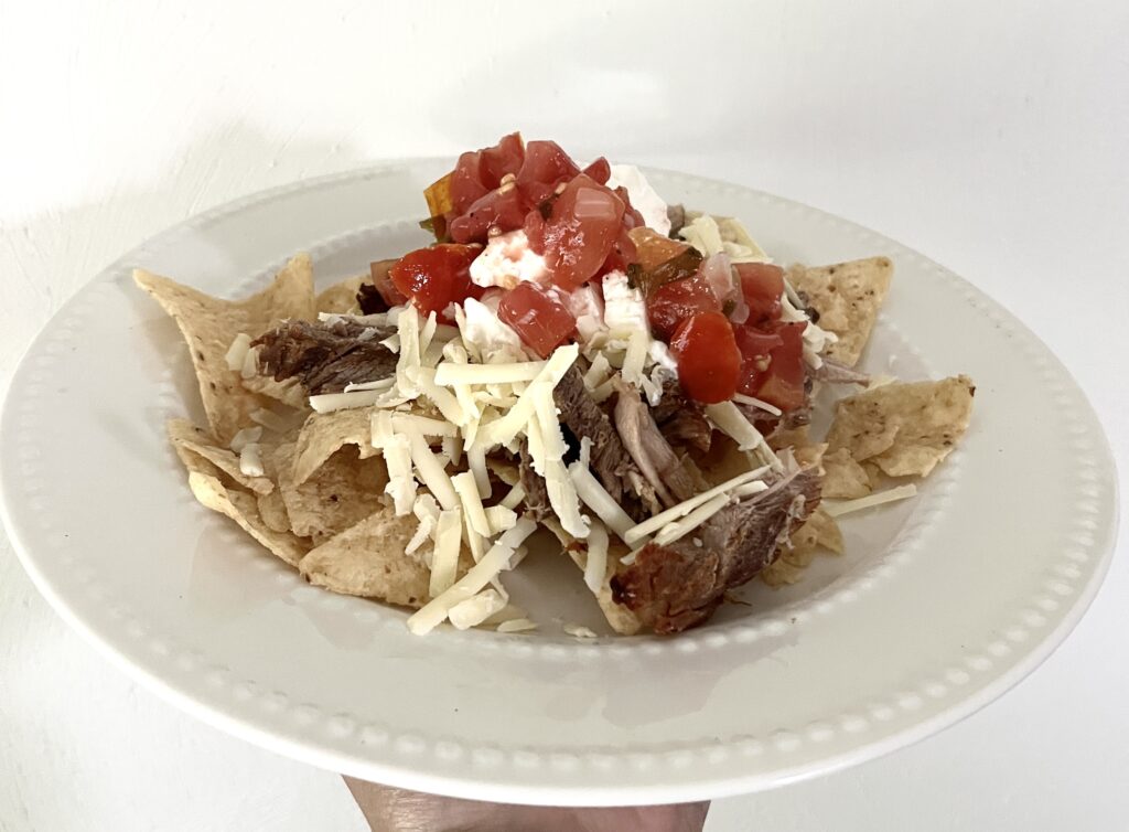 white plate of nachos topped with white cheddar cheese and femented salsa