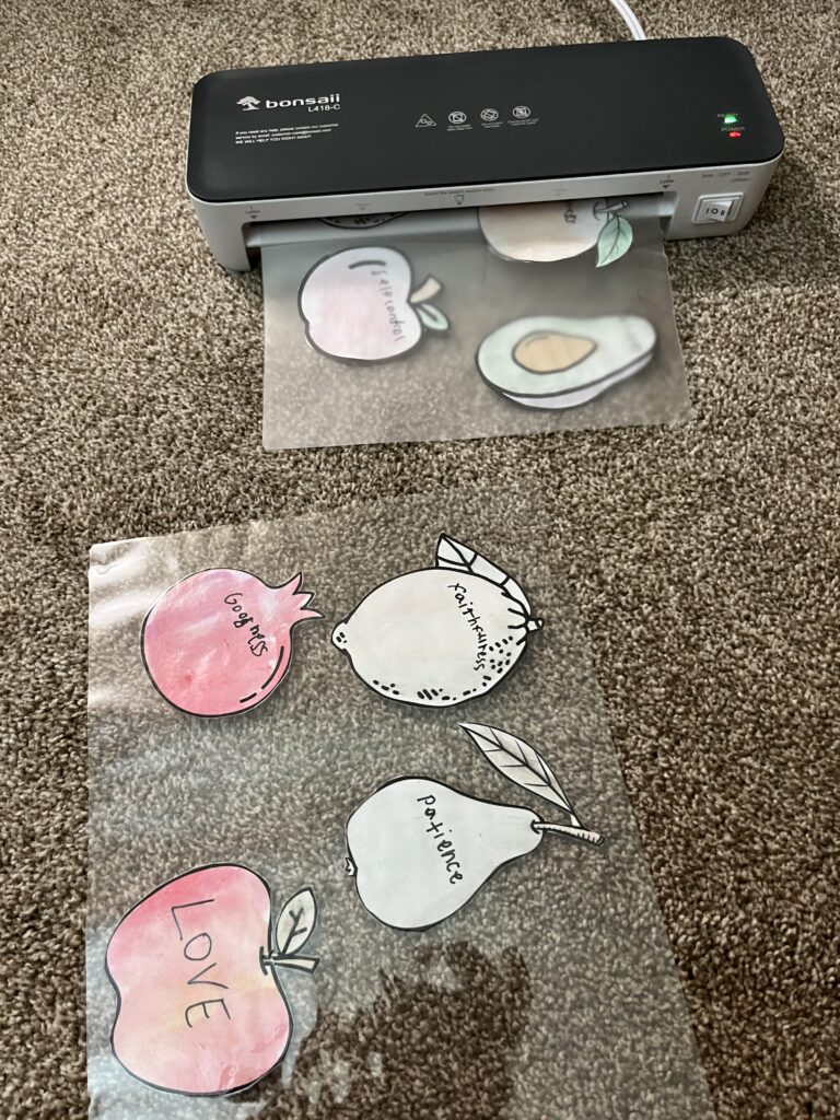laminating machine on carpeted floor running Fruit of the Spirit water color cut outs through machine