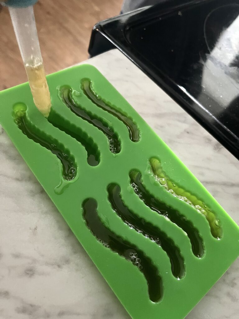 dropped adding liquid gummy candy mixture to green gummy worm mold