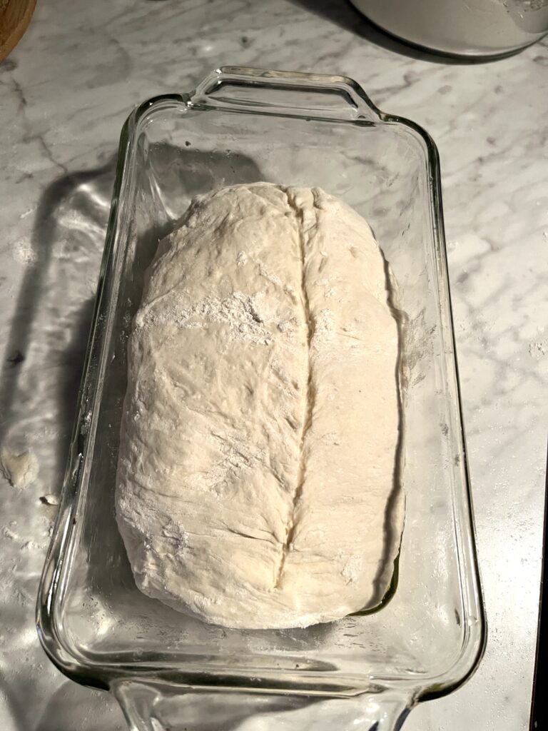 shaped sourdough in a glass loaf pan sitting on a marble counter