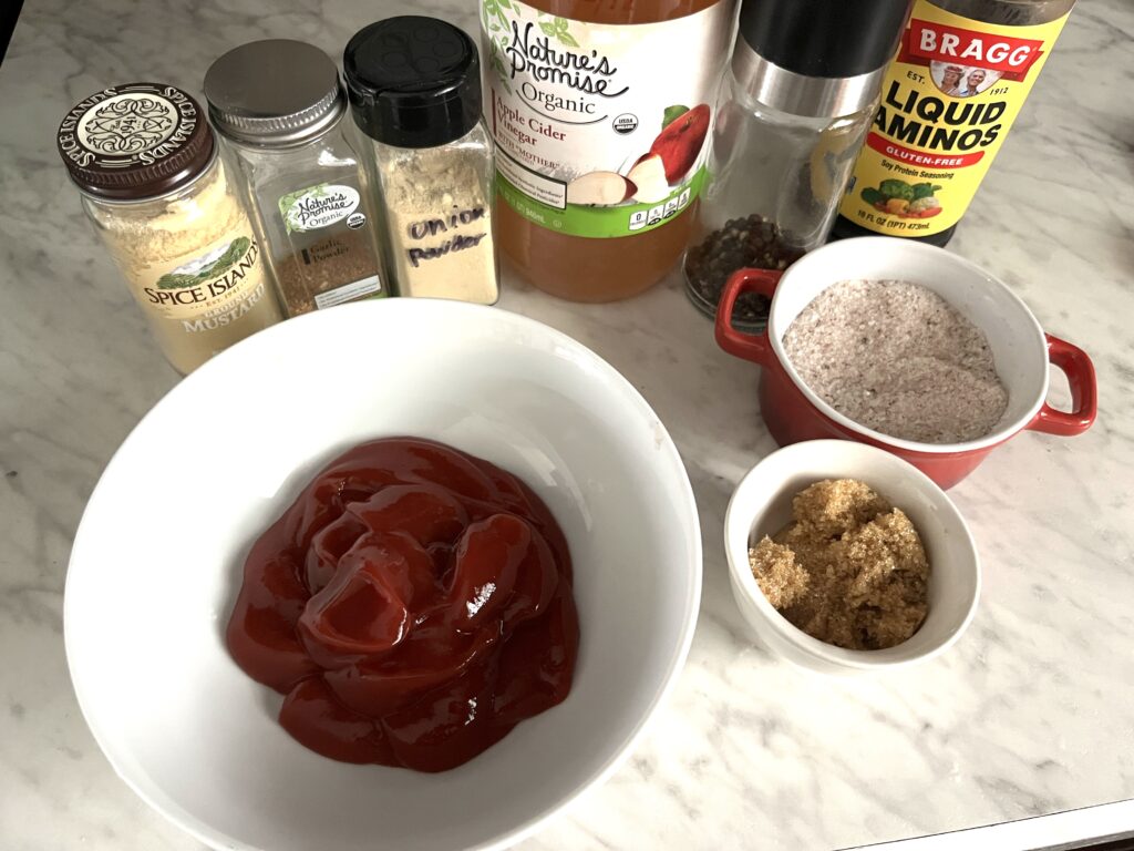 a white bowl of red bbq sauce and bottles of all the ingredients surrounding it on display