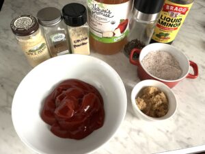 a white bowl of red bbq sauce and bottles of all the ingredients surrounding it on display