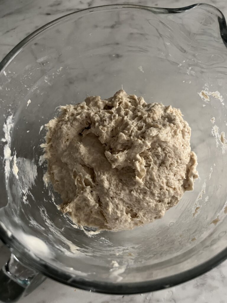 top view of a ball of sourdough pizza dough in a glass bowl on a white counter