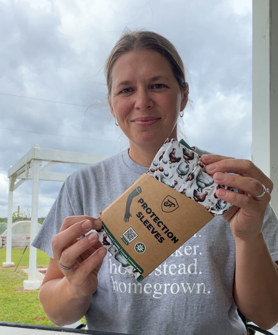 woman in gray shirt sitting outside on cloudy day holding cardboard packaged protection sleeves in chicken pattern towards the camera