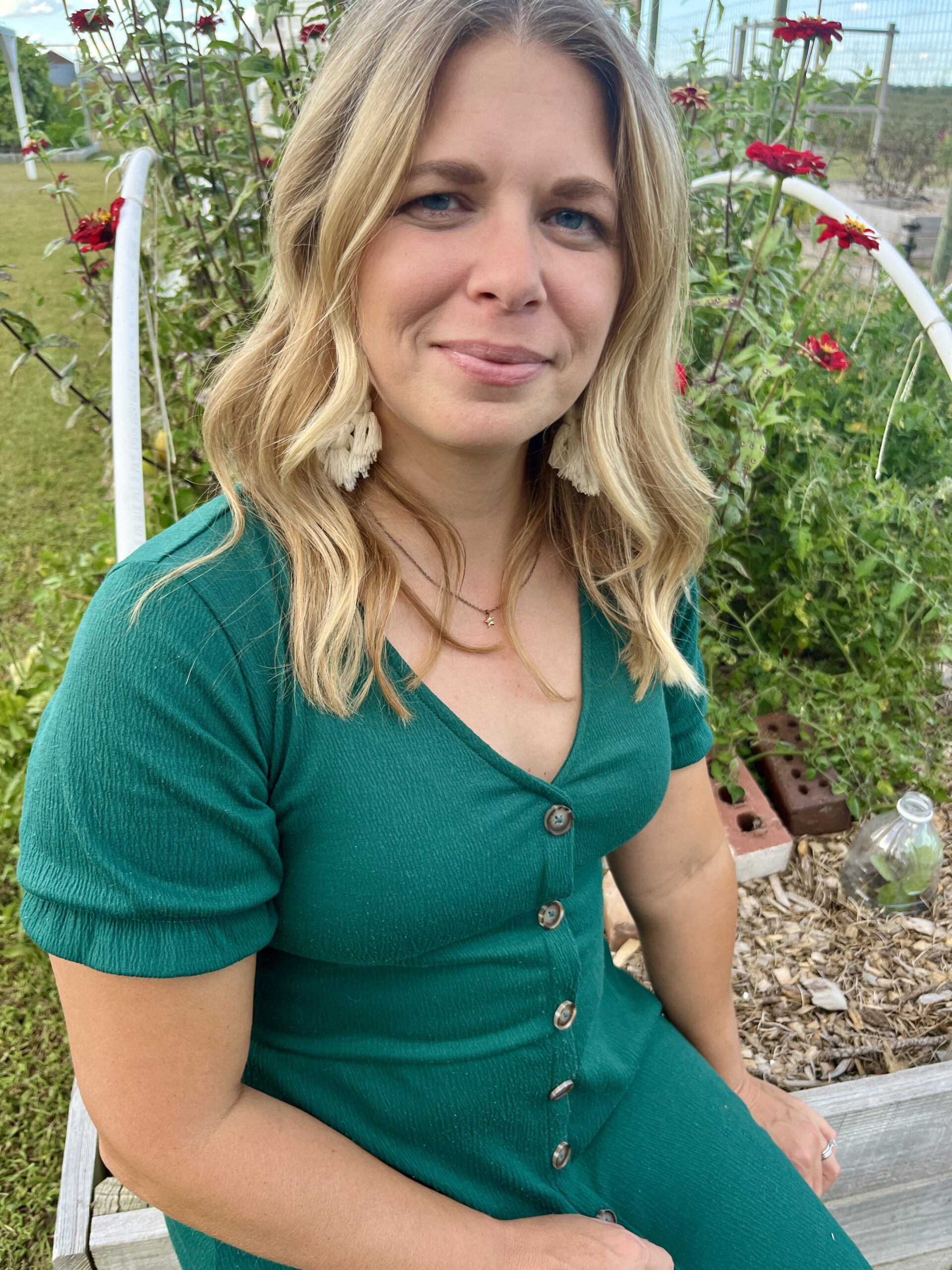 woman in green dress sitting on the edge of a garden bed with red zinnias in bloom behind her