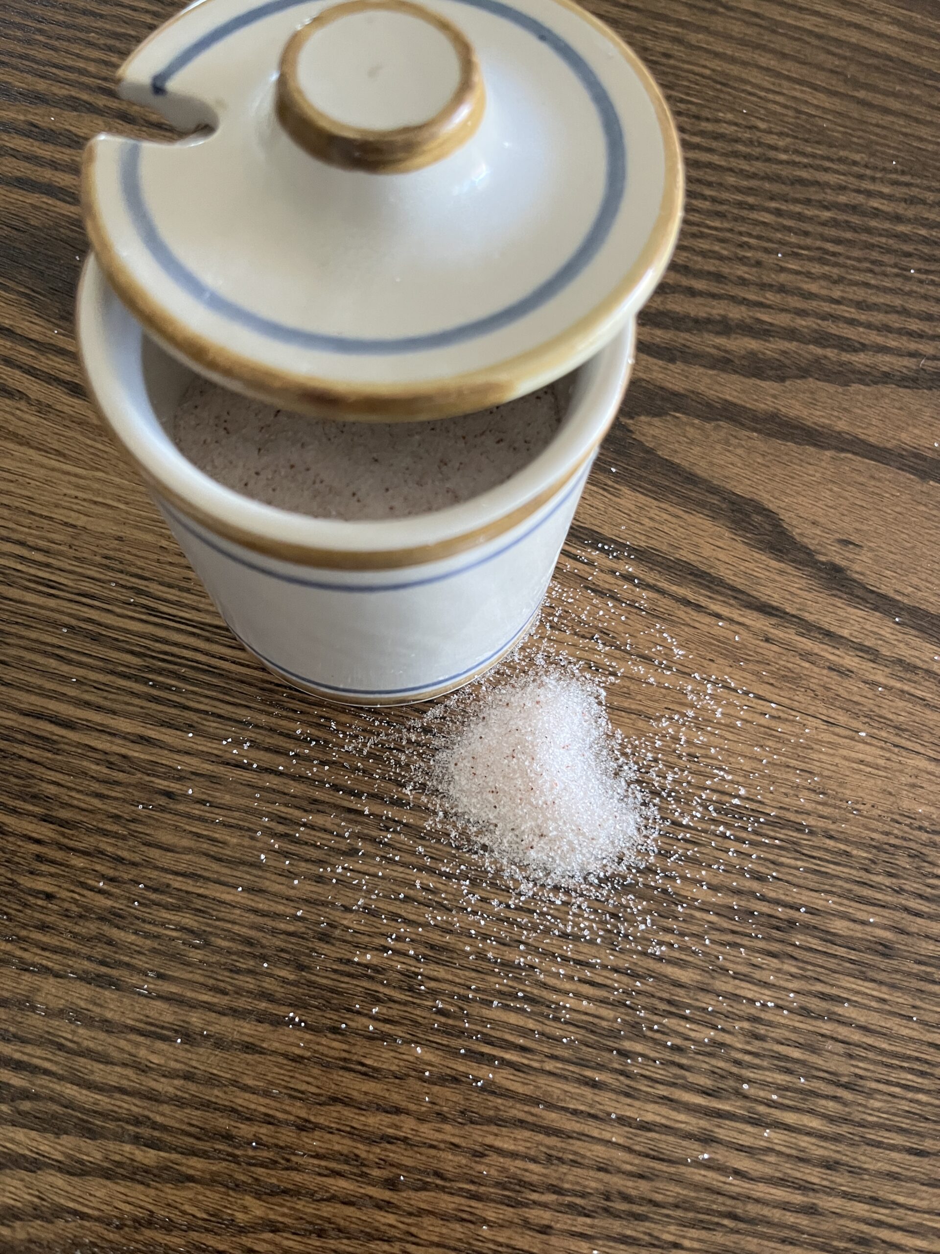 white, blue, and brown mini crock opened slightly to show pink real salt with some salt spilled down on brown wooden tabletop