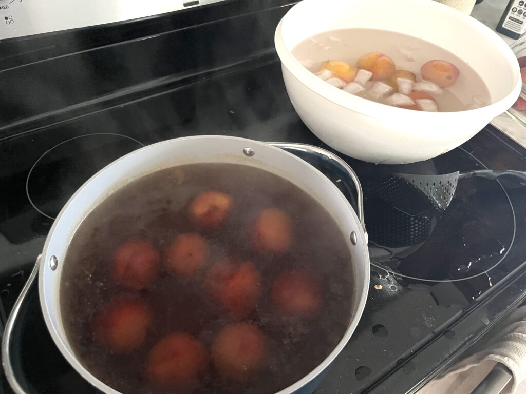 peaches being blanched in a pot with a white bowl ice bath in the background icing down blanched peaches to become peach jam