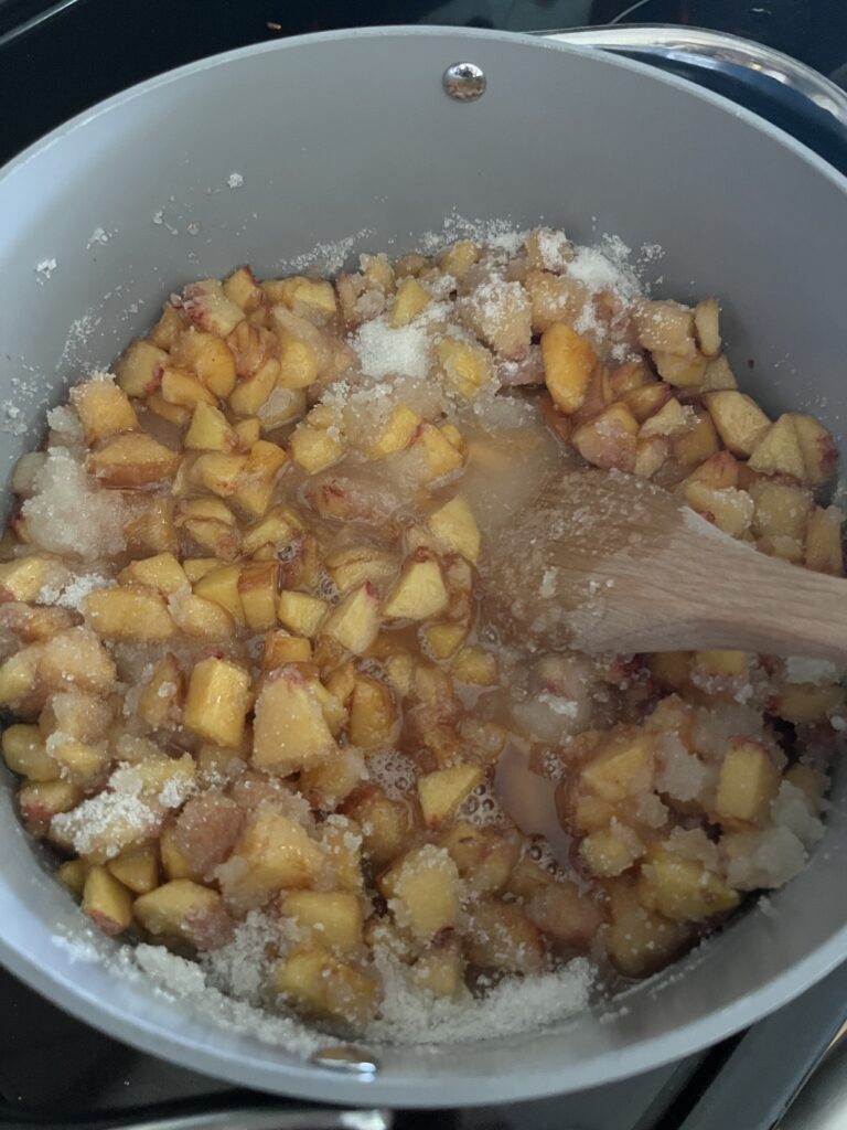a pot full of diced peaches being cooked down into peach jam