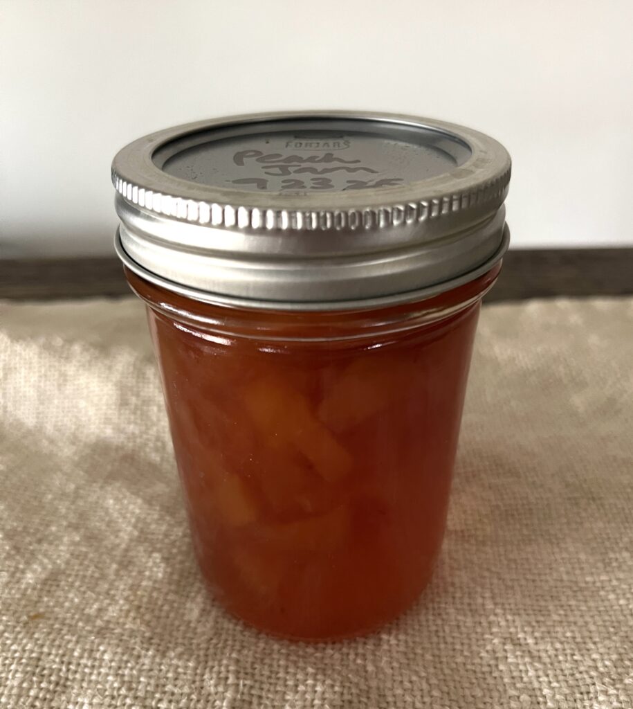 single half pint jar of peach jam sitting on a linen towel