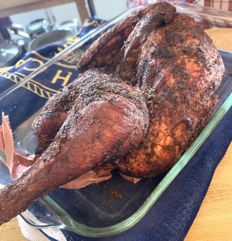smoked turkey covered in all meat seasoning in a glass roasting pan