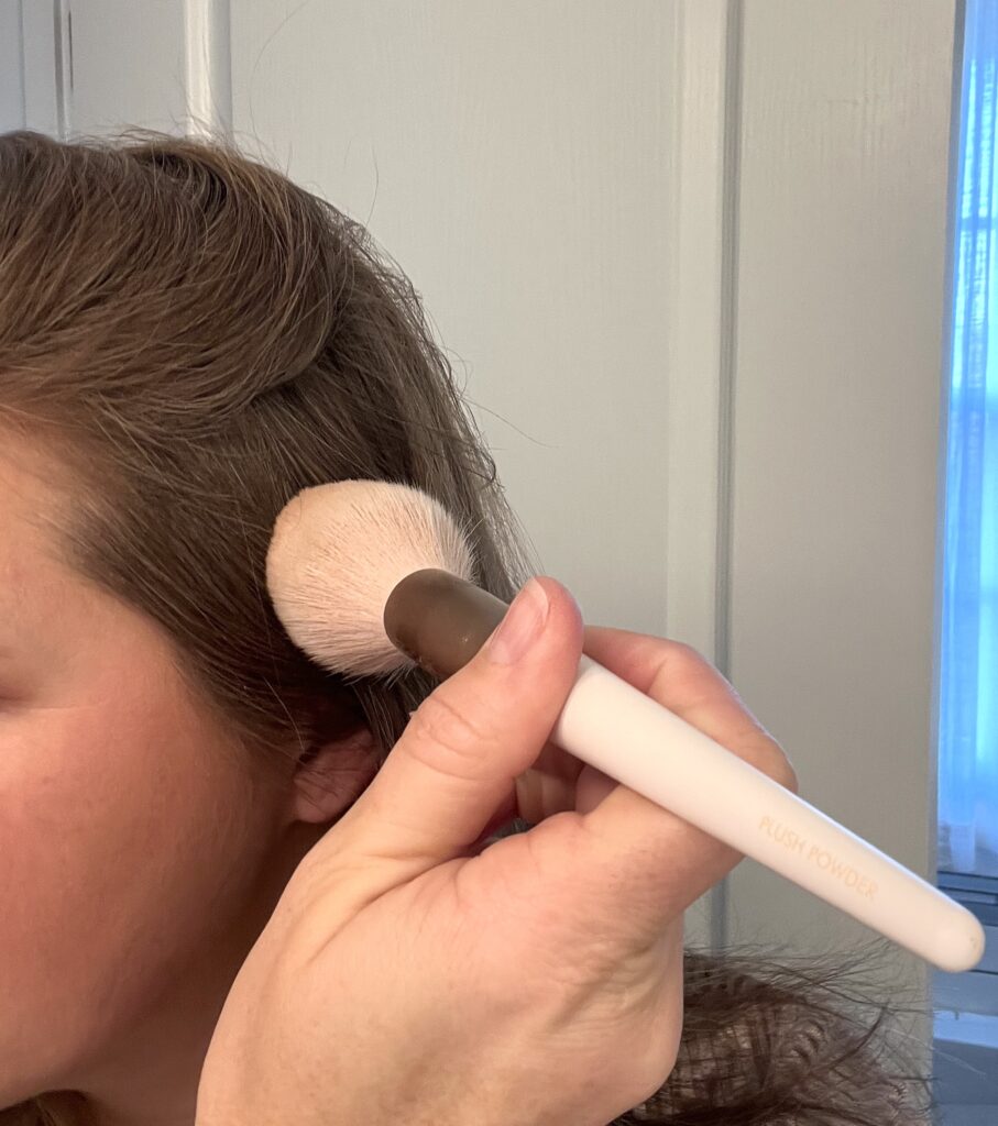 brown haired woman holding a blush powder brush to her scalp
