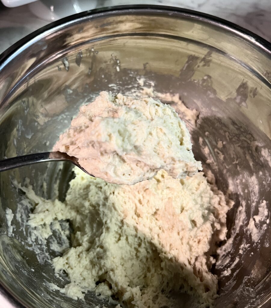silver spoon scooping out drop biscuit dough from a silver bowl