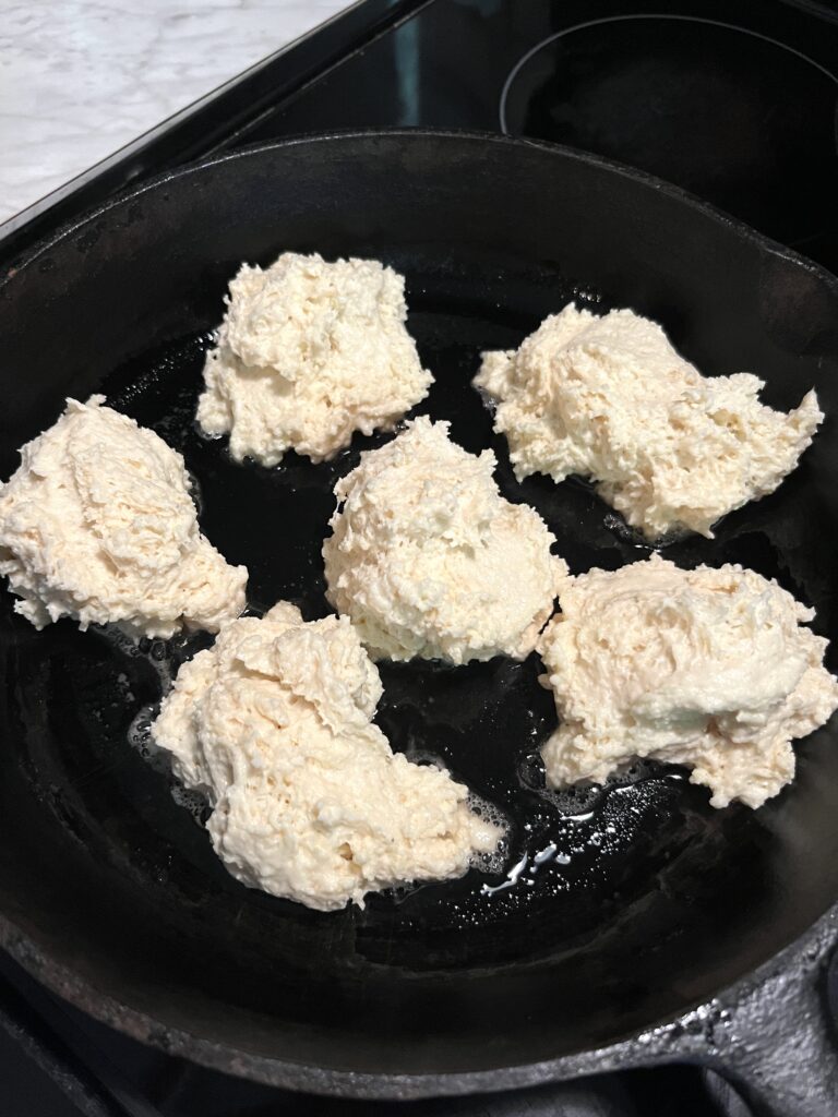 six dollops of sticky dough dropped into a cast iron skillet with grease to cook the bottoms