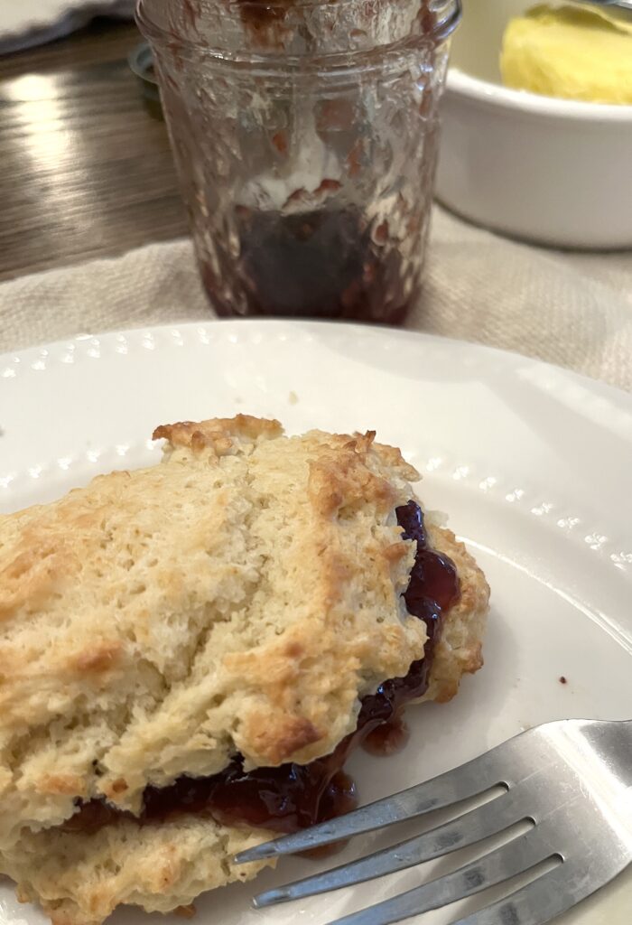 a white plate holding a golden brown drop biscuit split and filled with strawberry jam