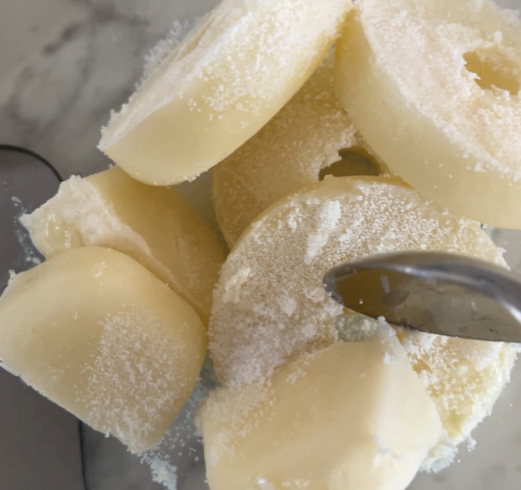 frozen goats milk ice cubes with lye sprinkled on top being stirred with a silver spoon to make tallow and goats milk soap