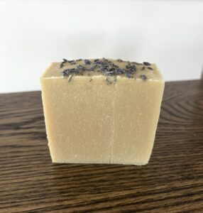 a single goats milk soap bar sitting on a wooden table with lavender buds sprinkled on top of the soap