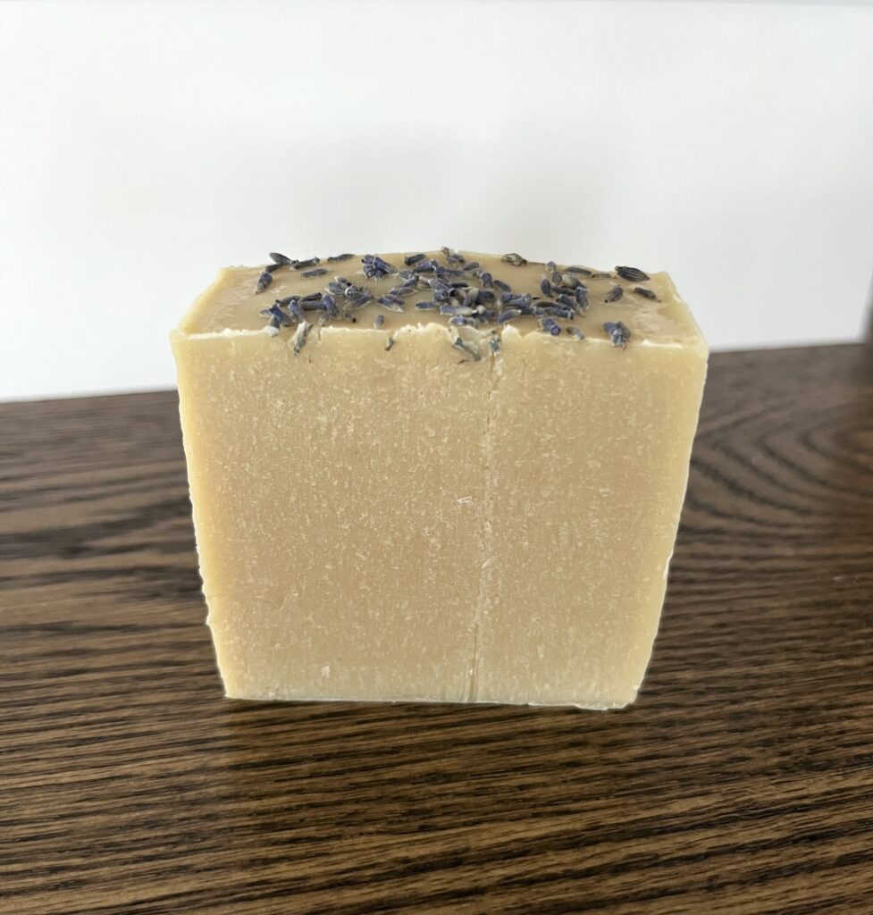 a single goats milk soap bar sitting on a wooden table with lavender buds sprinkled on top of the soap