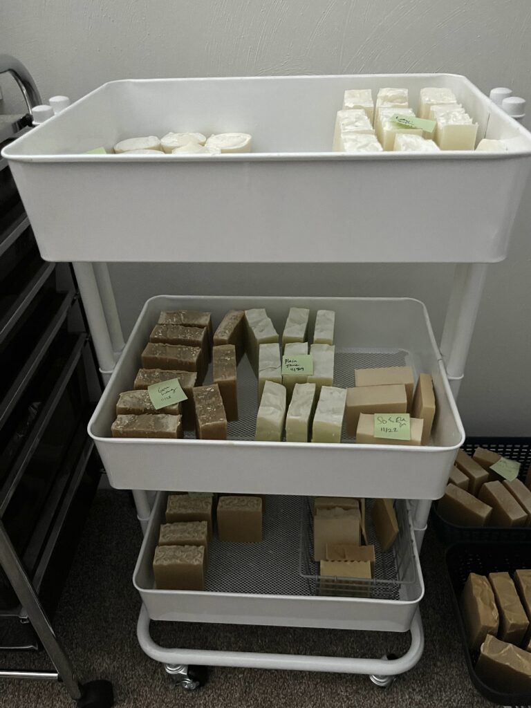 white three tier cart with many bars of homemade soap curing on the shelves