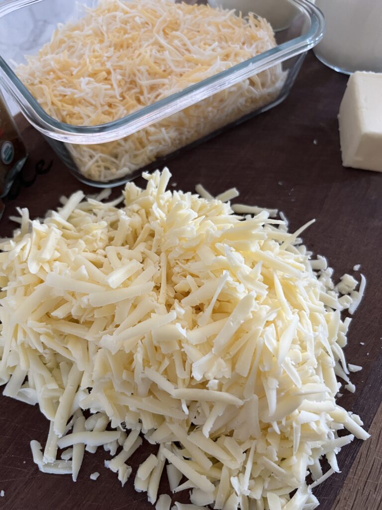 one pile of white shredded cheese in the forefront with a glass dish of yellow and white cheese in the background for smoked Mac and cheese