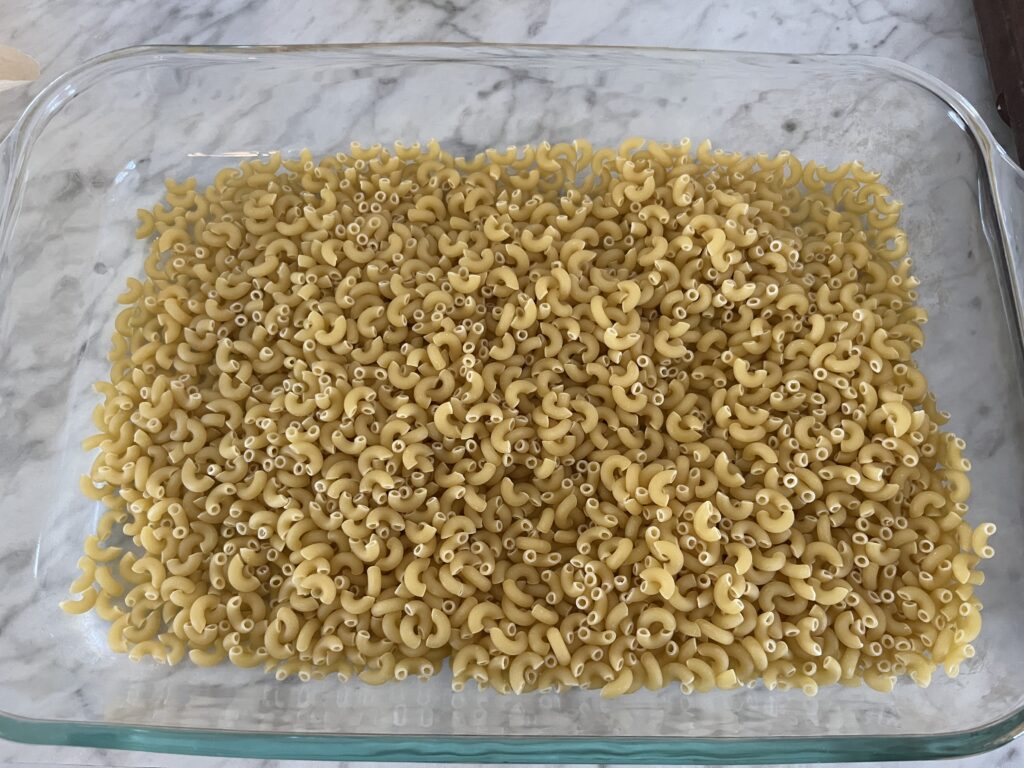 pan of dry macaroni noodles sitting on a white marble countertop