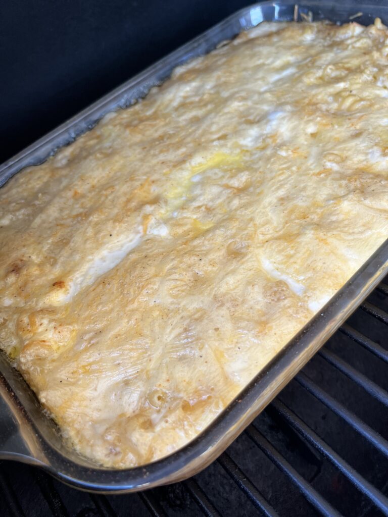 glass casserole dish of yellow and orange mac and cheese on a smoker grill