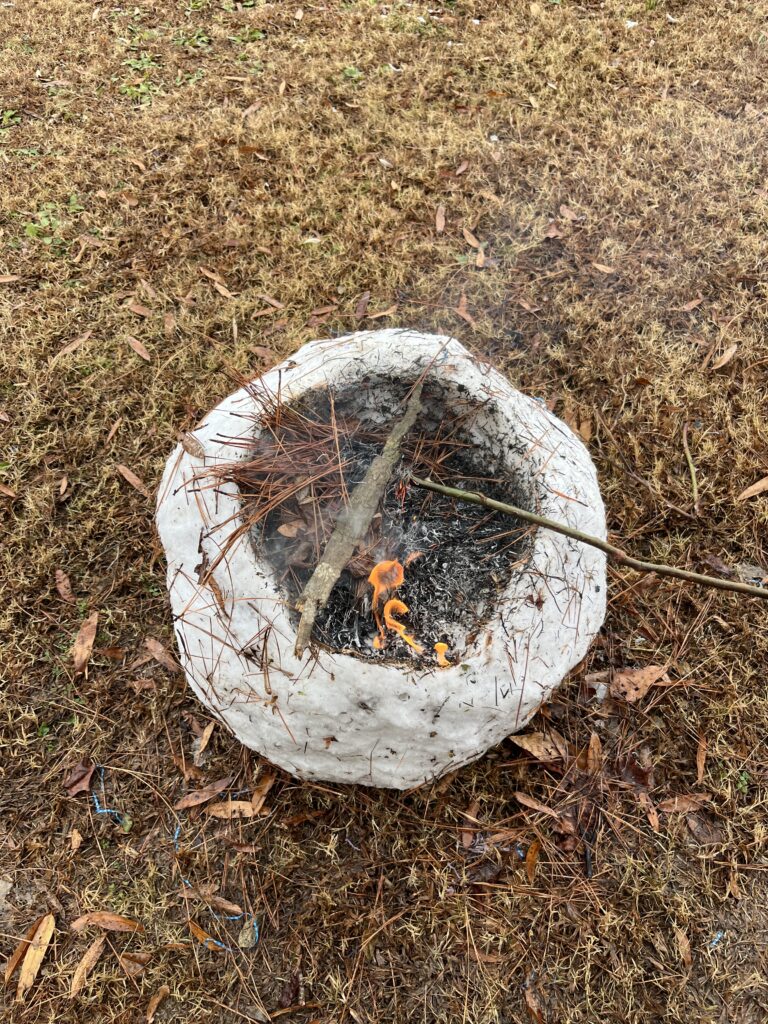 a ball of rolled up snow with a cave in the top being used as a make shift fire place with pine straw and sticks inside of the cave makes outdoor activities great for analog living