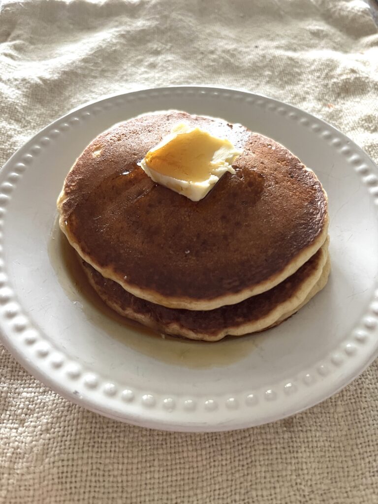 a double stack of freshly milled sourdough pancakes on a white plate sitting on a linen napkin in the morning light
