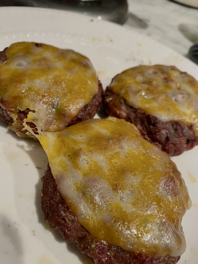 three grass fed burger patties topped with Colby jack cheese on a white plate