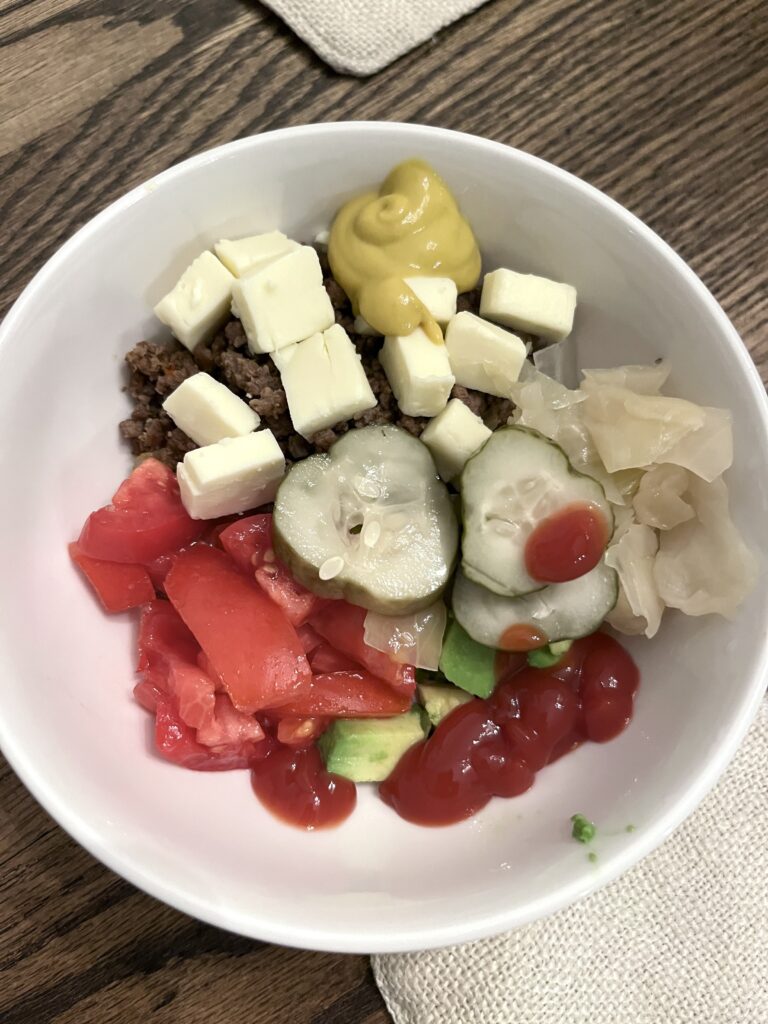 cooking from scratch made simple with a burger bowl in a white bowl with ground beef, cheese, mustard, ketchup, tomatoes, and pickles