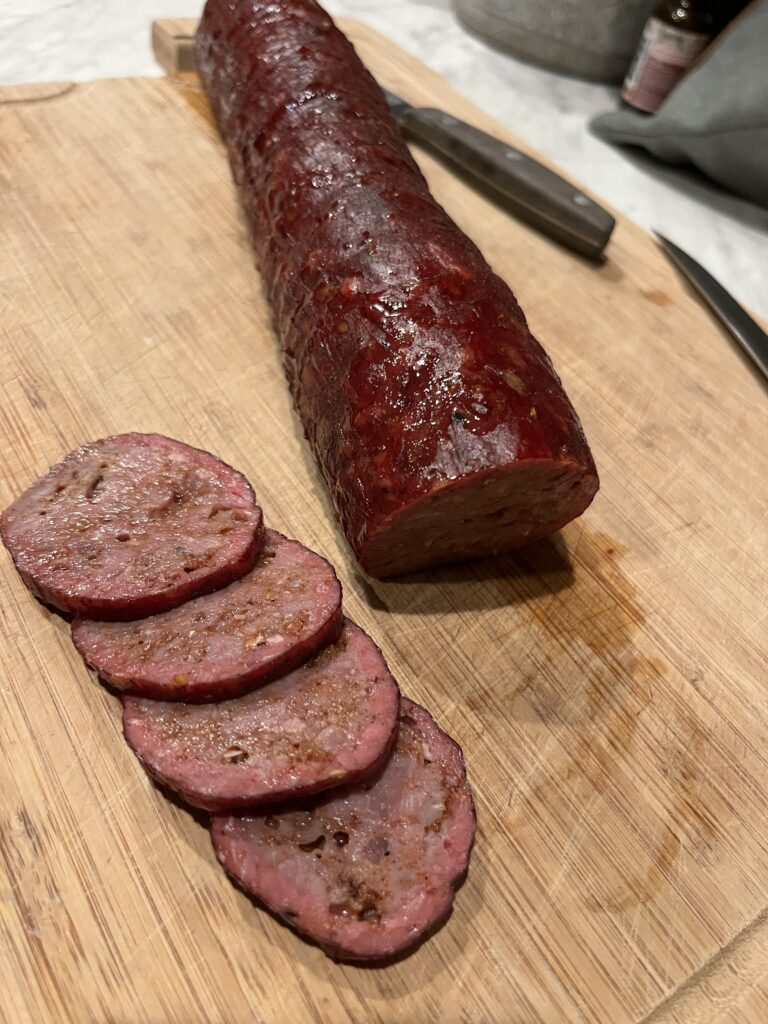 pepperoni meat stick on a wooden cutting board, half sliced into 4 rounds and the other half whole
