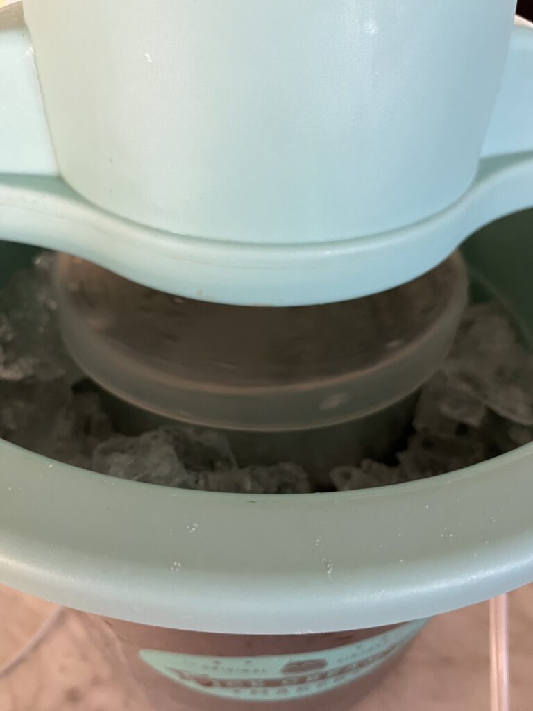 pale teal ice cream machine with an insert of ice cream mixture inside the machine surrounded by ice being churned