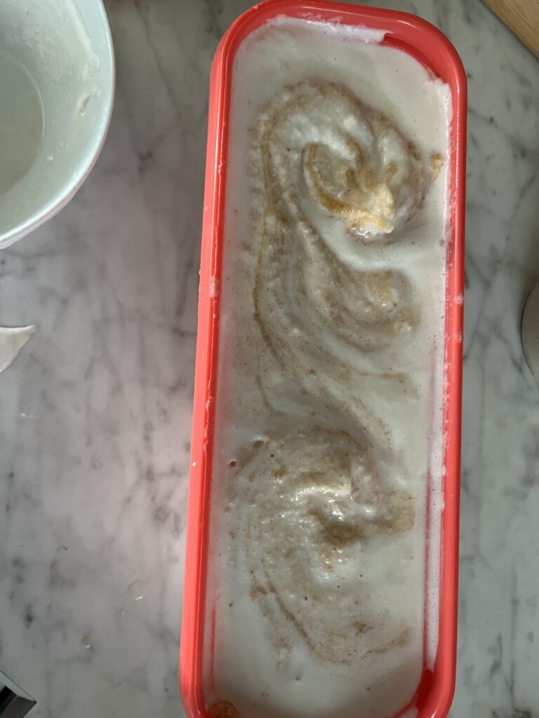orange ice cream container with orange colored fruit puree swirled into vanilla ice cream sitting on a marble counter top