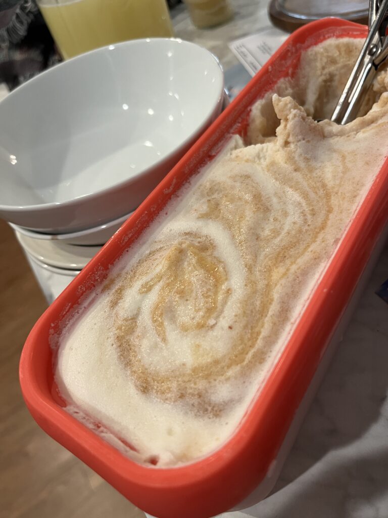 orange rectangle ice cream container in the foreground of photo with stack of white bowls in the background waiting for scoops of ice cream