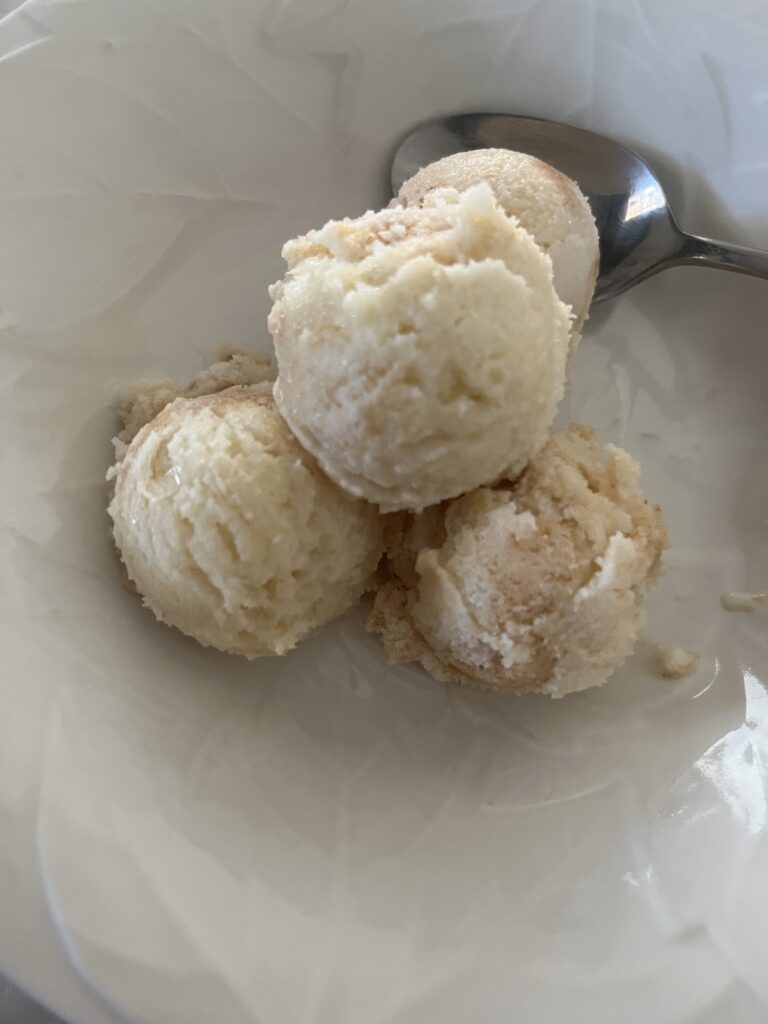 four small round scoops of ice cream in a white bowl with a silver spoon inside the bowl